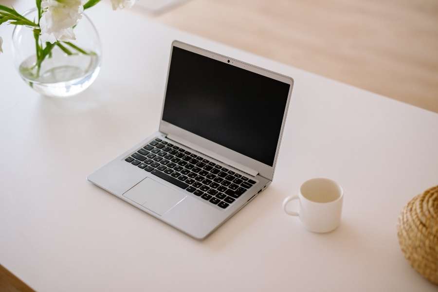 Un laptop argenté ouvert avec écran éteint posé sur un bureau blanc, signe que le laptop a besoin d'être remplacé.