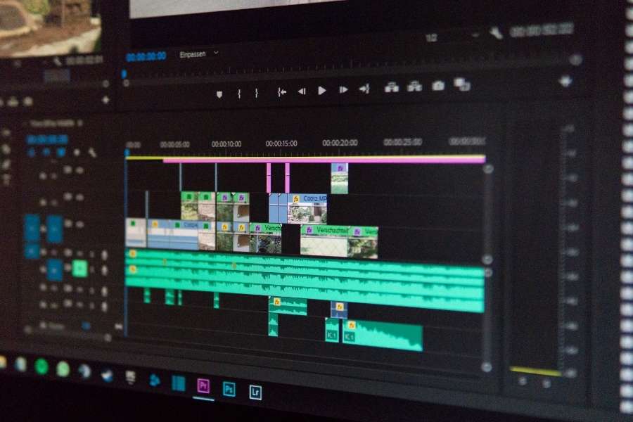 Une timeline de montage vidéo complexe s'affiche sur un écran avec plusieurs pistes audio et vidéo colorées.