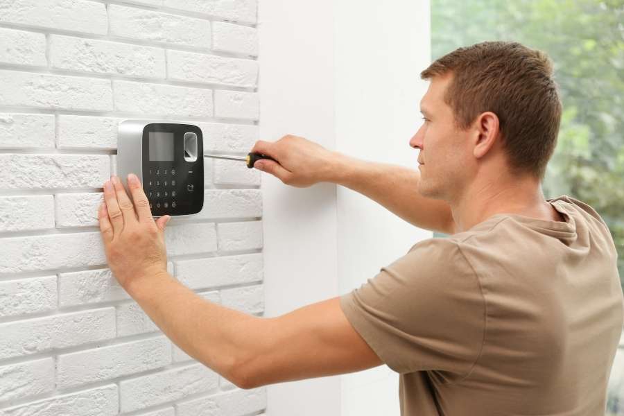 Un technicien utilise un tournevis pour installer le clavier mural d'une alarme ajax sans fil sur une cloison en briques blanches.