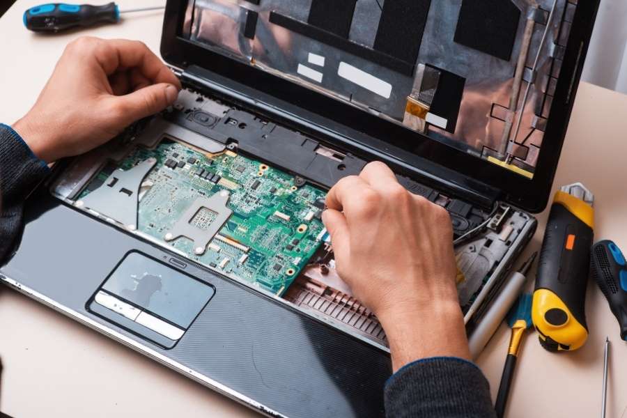 Un technicien manipule les composants internes et la carte mère verte d'un ordinateur portable ouvert.