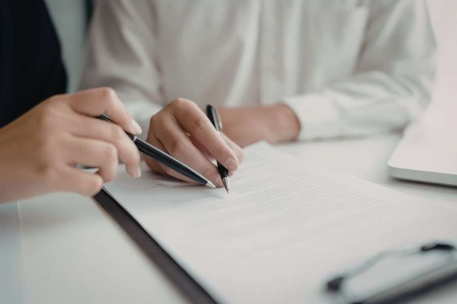Deux professionnels analysent et pointent du stylo les clauses d'un document juridique posé sur une table.