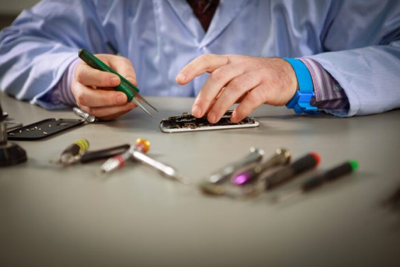 Gros plan des mains d'un expert réparateur de smartphone à Paris manipulant délicatement l'écran d'un téléphone en réparation avec des pinces de précision.