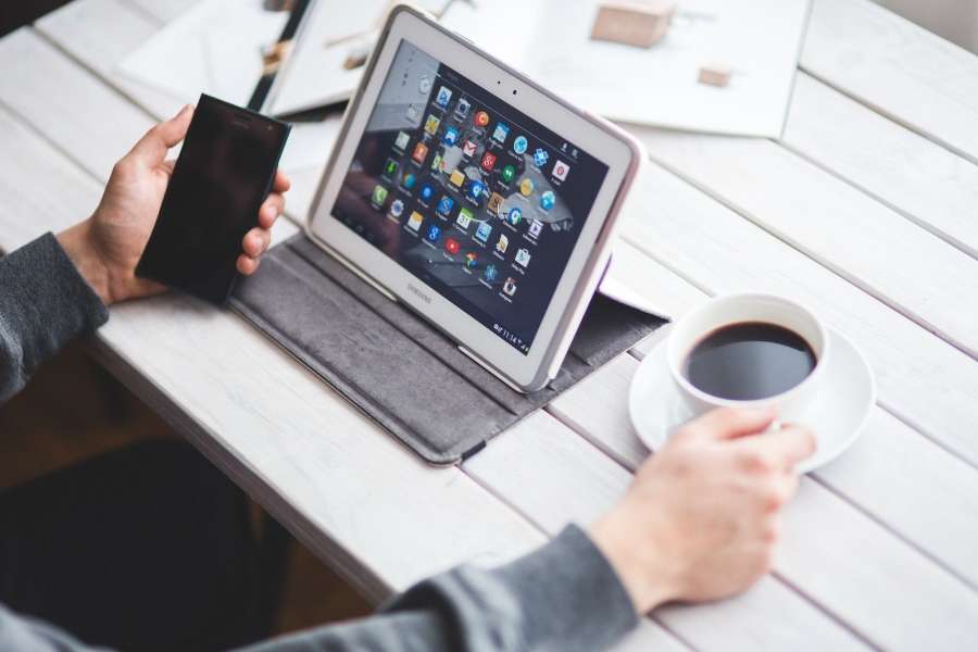 Une personne utilisant une tablette et un smartphone sur un bureau blanc pour sa communication digitale